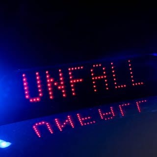 Das Blaulicht auf einem Fahrzeug der Polizei leuchtet in der Dunkelheit, während auf dem Display der Hinweis «Unfall» zu lesen ist. 