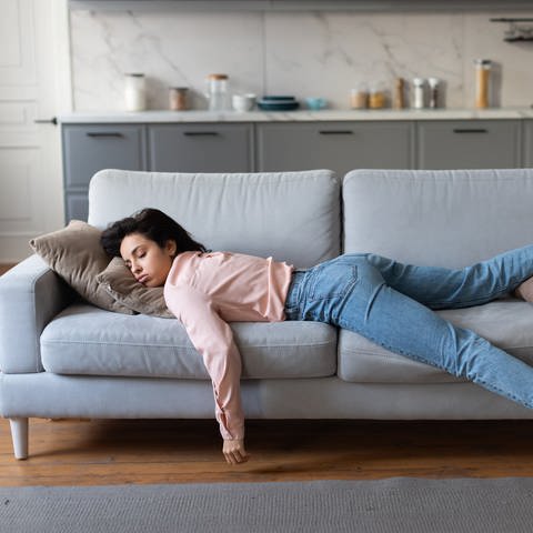 SYMBOLBILD: Eine Frau in rosa Bluse und Jeans liegt erschöpft auf der Couch. (Foto: IMAGO, IMAGO / Pond5 Images)