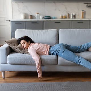 SYMBOLBILD: Eine Frau in rosa Bluse und Jeans liegt erschöpft auf der Couch. (Foto: IMAGO, IMAGO / Pond5 Images)